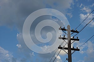 Old wooden electric pole on a blue cloudy sky background