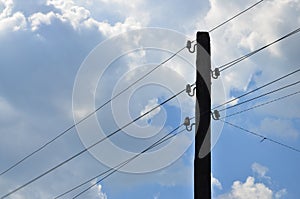 Old wooden electric pole for transmission of wired electricity on a background of a cloudy blue sky. Obsolete method of supplying