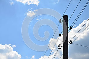 Old wooden electric pole for transmission of wired electricity on a background of a cloudy blue sky. Obsolete method of supplying