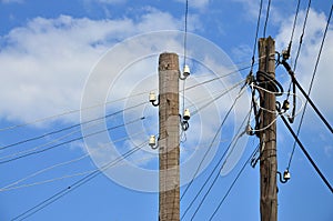 Old wooden electric pole for transmission of wired electricity on a background of a cloudy blue sky. Obsolete method of supplying