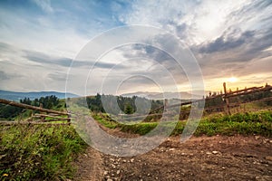 Old wooden fence, rural road and  top of mountain on horizon on sunset. summer autumn landscape