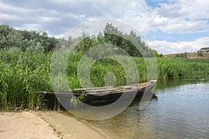 Old wooden fisherman boat on the river. Beautiful summer landscape with high reeds on the shore, lake and sky with clouds. Retro