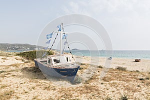 Old wooden fishing boat on the beach with Greek flags on the mast. Naxos island, Greece