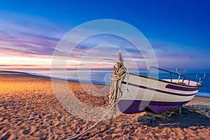 Old wooden fishing boat on beach at sunrise photo
