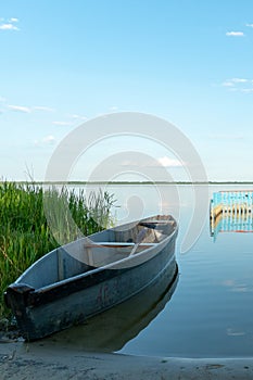 An old wooden fishing boat docked on a deserted sandy beach. View of a quiet and calm lake without ripples on the water.