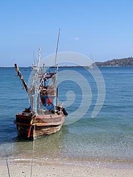 Old wooden fishing boat with light bulb for luring aquatic animals mooring on sand beach with sea and blue sky