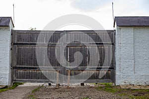 Old wooden gate with dirt road and two wooden balks in a gray brick fence.