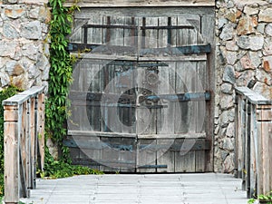 Old wooden gate with forged hinges in a stone wall