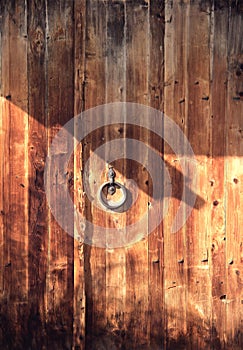 Old wooden gate with a metal door knob. Ring shape handle. Dark orange wooden background