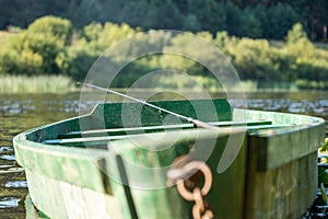 An old wooden, green boat on the river. Fishing rod with a float in the river. Fishing