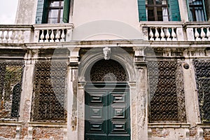Closeup of the facade of a building, on the streets of Venice, Italy. Antique wooden green door. Forged patterns on a