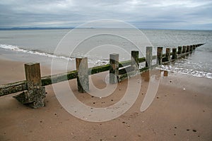 Old wooden groyne on empty, partially covered in sea water on co