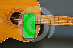 Old wooden guitar and phone with a green screen on a dark background