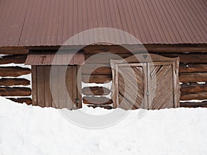 Old wooden house with closed shutters and a locked door is half buried in snow