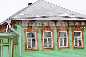 Old wooden house of green color with beautiful brown platbands on the windows