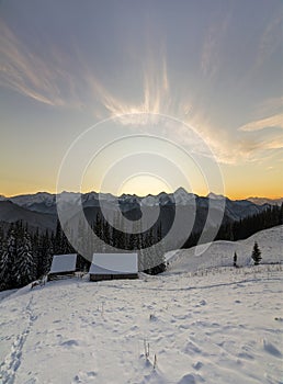 Old wooden house, hut and barn in deep snow on mountain valley, spruce forest, woody hills on clear blue sky at sunrise copy space