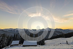 Old wooden house, hut and barn in deep snow on mountain valley, spruce forest, woody hills on clear blue sky at sunrise copy space