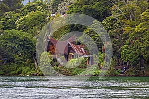 Old wooden house in a traditional Indonesian style with a fishing boat stands in a tropical forest