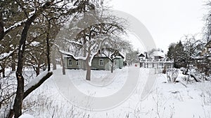 An old wooden house with old wooden window frames stands on a plot of land overgrown with grass and covered with snow in winter. A