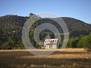 Old wooden hut at the edge of a forest beneath the mountains