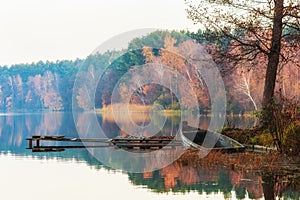 An old, wooden, leaky boat standing by the lake shore. In the background colourful trees