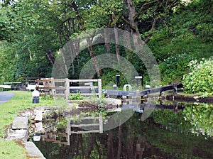 Old wooden lock gates with trees and flowers reflected in the water with mooring posts and fences on the rochdale canal at rawden