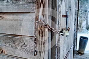 Old wooden outdoor bathroom secured with rusty chain and long shackle padlock