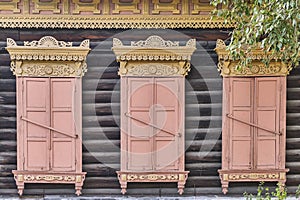 Old wooden painted windows. Carved yellow architraves, closed coral shutters. Ulan-Ude,Russia.