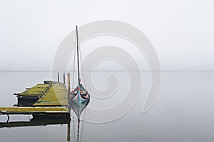 An old wooden pier and a brightly painted fishing boat next to it on the background of a foggy Atlantic ocean bay