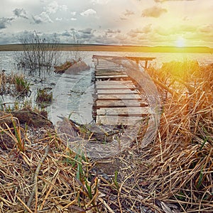 Old wooden pier with dry reed on sunset