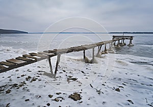 An old wooden pier in winter on a frozen lake goes into the distance