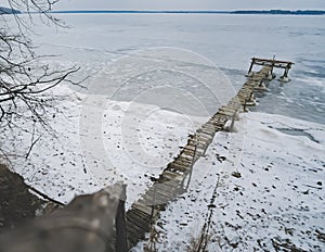 An old wooden pier in winter on a frozen lake goes into the distance