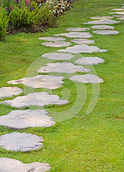 The old wooden plank-shaped garden path made of artificial stone material on green lawn with ornamental bush in public park area