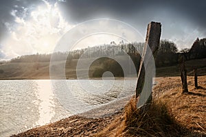 Old wooden poles on the shore of a lake with sun reflections, la