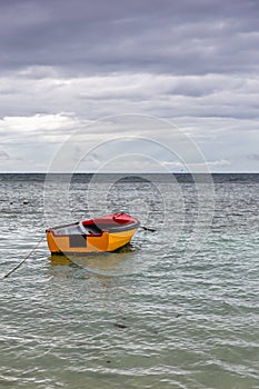 Old wooden red and orange fishing boat anchored at Baie Lazare Public Beach on Mahe Island, Seychelles, overcast cloudy sky