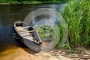 Old wooden rowing boat tied with chain and padlock at green summer bank on Neman river in Grodno Belarus
