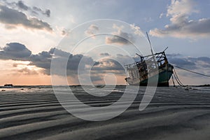 The old wooden ruined fishing boat set aground on the beach at Sunset time