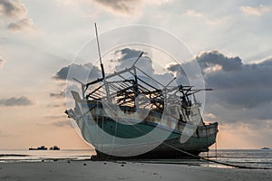 The old wooden ruined fishing boat set aground on the beach at Sunset time