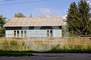 Old wooden rural house behind a wooden fence in the vegetation
