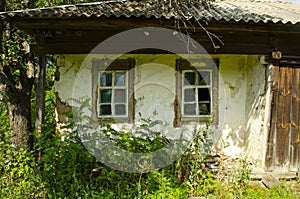 Old wooden rustic house plastered with clay and painted with white clay among flowering meadow grasses. House with cracked clay