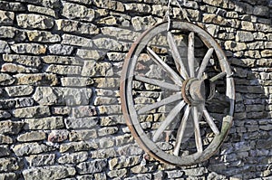 Old wooden rustic wagon wheel on a stone wall with hub and spokes