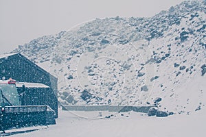 Old wooden shed by a rocky slope in heavy snowfall. Blizzard in the mountains. Extreme winter weather