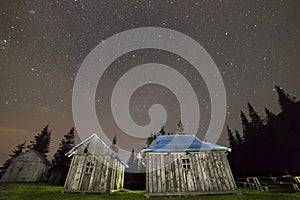 Old wooden shepherd huts on mountains clearing under starry sky. Wide angle, copy space background.