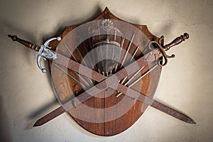 Old wooden shield with two rusty swords and a fencing helmet