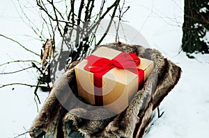 Old wooden sleigh with a gift in golden paper box wrapped red gift ribbon, are in the winter forest, snow, trees near. Wooden sled