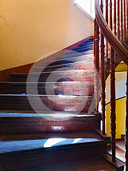 Old wooden spiral stairs highlighted by sun from behind the window