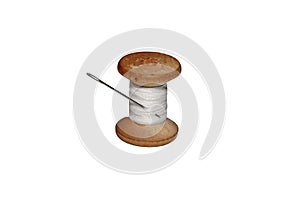 Old wooden spool of white thread and a metallic needle on a whit