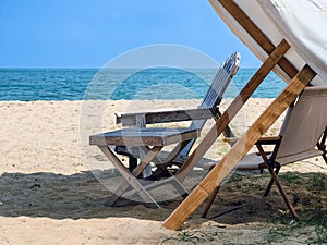 Old wooden table and beach lounge chairs under tent at tropical beach with beautiful turquoise ocean water, white sand and blue