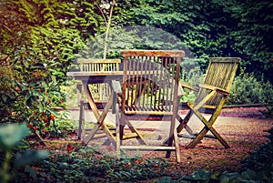 Old wooden table and chairs in the green garden of country house. Holidays in countryside in fresh air.