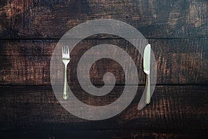 Old wooden table with fork and knife waiting for a dish of missing food, concept of summer diets